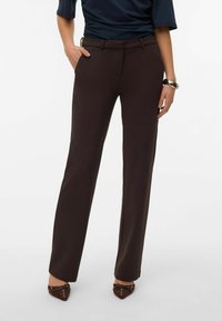 Brune, skreddersydde bukser med glatt tekstur, rette ben og beltehemper; kombinert med en marineblå topp og brune, spisse sko.