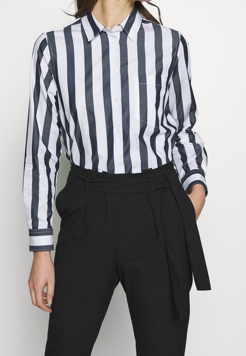 Knapp-up skjorta med blå och vita vertikala ränder, långa ärmar, krage och en bröstficka, ihop med högmidjade svarta byxor.