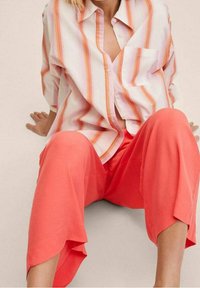 Gestreepte overhemd in wit, oranje en roze, gecombineerd met koraalkleurige wijde broek. Textiel met structuur, ontspannen pasvorm en zijzakdetails.