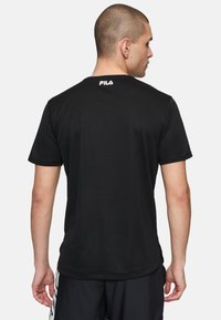 Camiseta negra de manga corta hecha de tejido suave. Presenta un escote redondeado y un pequeño logo blanco en la parte de atrás.