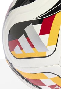 Dettaglio di un pallone da calcio Adidas bianco con motivi geometrici neri, rossi e gialli e il logo Adidas in argento.