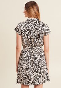 Kleid mit Leopardenmuster, kurzen Ärmeln, kragenförmigem Ausschnitt, tailliertem Gürtel und ausgestellt Rock. Der Stoff hat eine glatte Textur mit einem hellbeigen Hintergrund.
