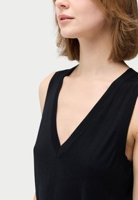 Svart ärmlös topp med djup V-ringning, gjord av mjukt tyg. Har ribbade kanter längs ringningen och ärmhålen.