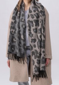 Personne portant un manteau beige et une écharpe gris léopard à franges sur une tenue gris clair.