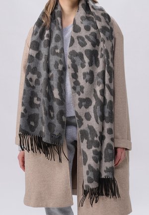 Personne portant un manteau beige et une écharpe gris léopard à franges sur une tenue gris clair.