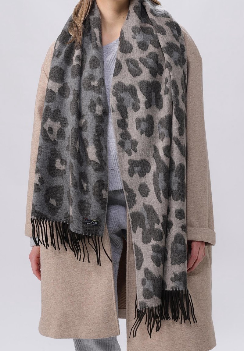 Personne portant un manteau beige et une écharpe gris léopard à franges sur une tenue gris clair.