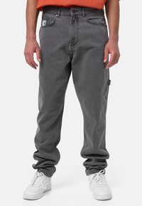 Harmaat farkut, joissa on rento leikkaus, viisi taskua ja etuosassa logo-patch. Yhdistettynä valkoisiin tennareihin.