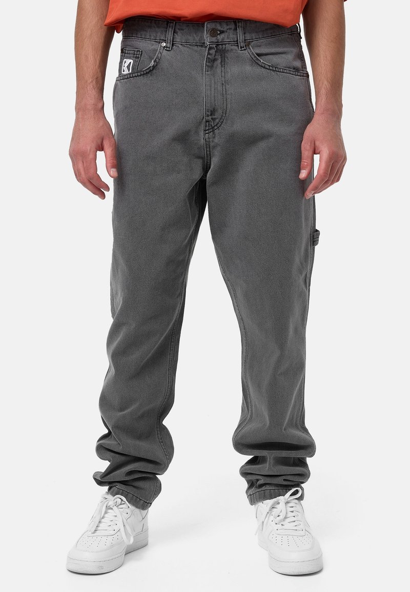 Harmaat farkut, joissa on rento leikkaus, viisi taskua ja etuosassa logo-patch. Yhdistettynä valkoisiin tennareihin.