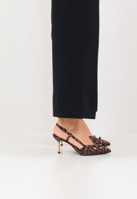 Escarpins slingback à imprimé léopard avec bout pointu, accents dorés et talon élancé. Le matériau semble doux avec une texture lisse.