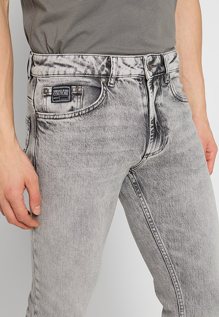 Jeans in denim grigio con un lavaggio sbiadito, vestibilità regolare, design a cinque tasche, etichetta con marchio sul retro e dettagli in hardware color argento.