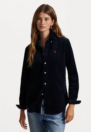 Dark navy corduroy shirt with long sleeves, button-down collar, and white buttons; small red logo on left chest. Casual design, relaxed fit.