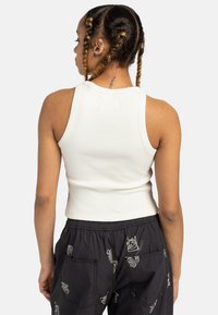 Hvid ribbet tanktop med rund hals, tætsiddende design og cropped længde, parret med sorte bukser med kattemønster.