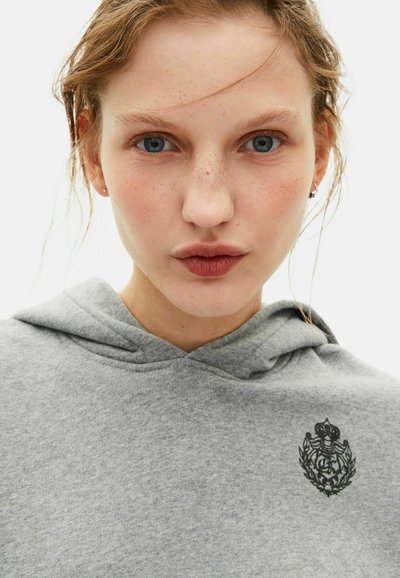 Felpa grigia con cappuccio, tasca frontale ed emblema nero con design di corona e alloro sulla zona sinistra del petto. Tessuto liscio.
