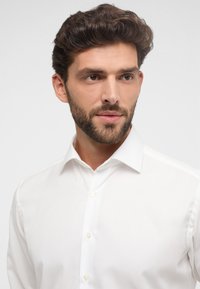 Camicia da uomo bianca a maniche lunghe con colletto classico, chiusura con bottoni e texture liscia. Vestibilità standard e design pulito, adatta per abbigliamento formale.
