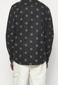 Zwart shirt met lange mouwen, met een subtiel, fijn patroon in crème. Knopdetails aan de manchetten, textuurstof.