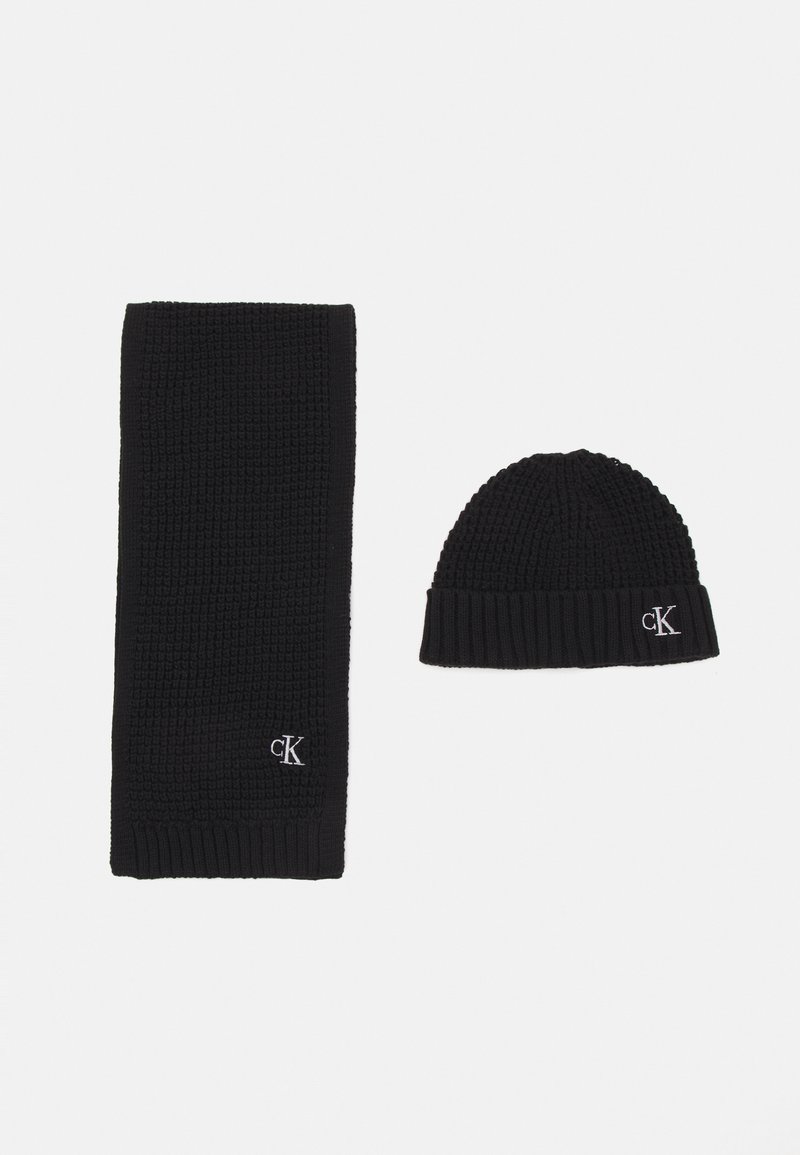 Conjunto de cachecol e gorro de malha preta, com textura canelada e logótipo bordado. Ambos os itens têm um design de cor sólida.