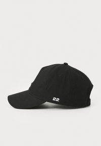 Svart baseball cap laget av stoff med buet visir. Har brodert "22" detalj på siden og en knapp på toppen.