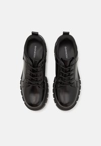 Zwarte veterschoenen met een glanzende afwerking, rubberen zool, gevoerd enkeldeel en subtiel logo op de binnenzool. Eenvoudig ontwerp, geen patronen of accenten.
