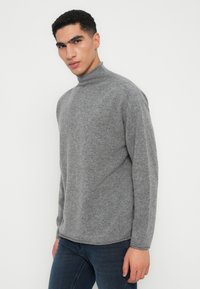Sweater cinza de gola alta feito de um tecido macio e texturizado. Apresenta um corte descontraído e mangas longas, com um acabamento suave e gola dobrada.