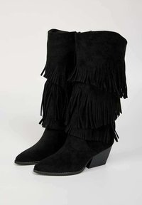 Bottines en suede noir avec des franges multilayer, des bouts pointus et un talon carré. La texture est douce avec une finition lisse.