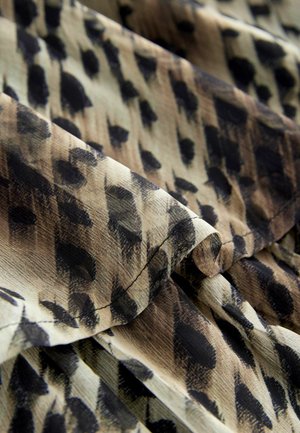 Tlačená látka s abstraktným čiernym a hnedým vzorom na svetlobéžovom pozadí; hladká textúra s jemnými záhybmi a prehýbaniami.