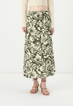 Lange groene rok met witte botanische print, voorzien van een gestrikt tailleband en een vloeiend ontwerp. Gecombineerd met tan hakken met banden.