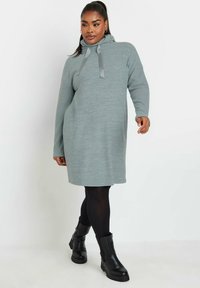 Ljusgrå stickad klänning med huva, med långa ärmar och en avslappnad passform. I kombination med svarta ankelboots och strumpbyxor.