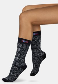 Kniestrümpfe in Schwarz mit weißen geometrischen Mustern. Gerippte Oberseite mit buntem Detail der isländischen Flagge. Strukturierter Stoff für Komfort.