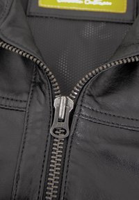 Schwarze Lederjacke mit silbernem Metallreißverschluss, detaillierter Nähtechnik und einer strukturierten schwarzen Innenauskleidung. Etikett sichtbar im Kragen.