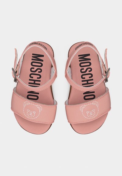 Ροζ σανδάλια με ανοιχτό δάχτυλο και ρυθμιζόμενα λουριά στον αστράγαλο, με κέντημα λευκής αρκούδας στα εμπρόσθια λουριά και το γράμμα «MOSCHINO» τυπωμένο στις εσωτερικές σόλες.
