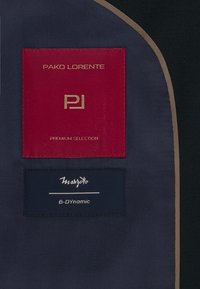Nawojowe etykiety materiałowe mają czerwone i ciemnoniebieskie sekcje z złotym i białym tekstem. Etykiety zawierają napisy „Pako Lorente”, „Premium Selection” i „B-Dynamic.”