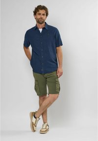 Korte mouwen, donkerblauwe button-up shirt, kaki cargoshorts en beige sneakers met donkere accenten; casual outfit geschikt voor warm weer.