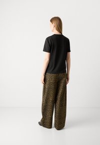 Top corto nero a maniche corte abbinato a pantaloni a gamba larga con stampa leopardo in marrone e nero, caratterizzati da una texture liscia e una vestibilità comoda.