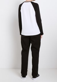 Sort og hvid langærmet skjorte med raglanærmer, lavet af bomuld. Båret med sorte bukser og hvide sneakers.