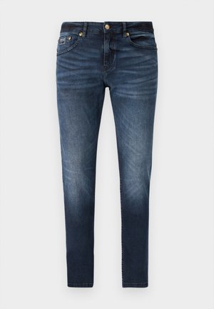 Dark blue denim jeans with a straight leg design, featuring a medium wash, gold-tone hardware, and a logo patch on the back pocket.