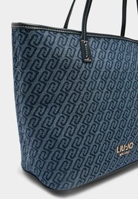 Borsa tote in denim blu con motivo a logo ripetuto, caratterizzata da dettagli in pelle nera e un logo dorato alla base.