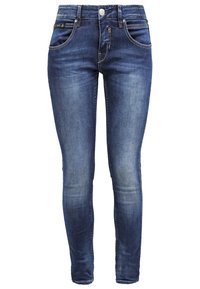 Blå urblekta skinny jeans med framfickor, bälteshällor och knappstängning på vit bakgrund.