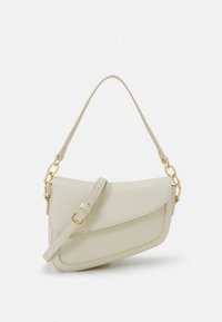 Jasnobeżowa skórzana torebka o zaokrąglonym kształcie, wyposażona w górną klapę, odpinany pasek i ozdoby w kolorze złotym.