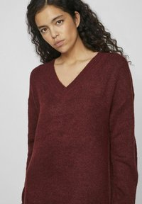 Pull en V burgogne avec un tricot texturé, manches longues et coupe ample. Prévient le confort et la chaleur dans son design.