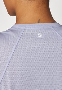 Heled lilla spordipaita, millel on võrguline tekstuur, ümmargune kaelus ja väike logo seljal, kaela lähedal.