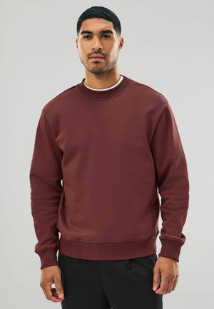 Hanorac de culoare vinie, cu guler și manșete cordonate. Fabricat dintr-un material moale, având o croială lejeră și o textură fină, asortat cu pantaloni negri.
