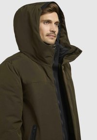 Dark green insulated jacket with a high collar and oversized hood, featuring a zippered front and side pockets, made from a smooth, matte fabric.