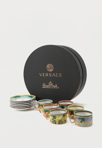 Ensemble de sept tasses à thé ornées de Versace Rosenthal avec soucoupes assorties, présentant des motifs baroques colorés, exposées à côté d'une boîte ronde noire.