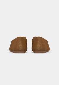 Paire de chaussures en daim marron sans lacets vues de dos sur une surface blanche unie.