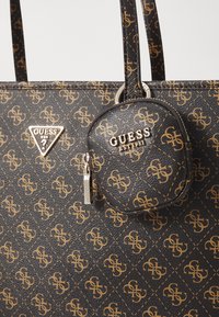 Black synthetic tote bag with gold logo pattern, featuring a round coin purse attached. Includes a triangular silver logo accent.