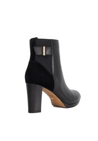 Black ankle boot featuring a smooth leather upper, velvet side panel, and a block heel. Includes a decorative bow and gold-tone accent.
