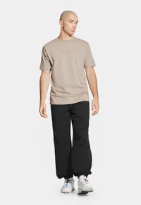 Beżowa bawełniana koszulka z subtelnym logo, zestawiona z czarnymi spodniami cargo i szarymi trampkami z wyraźnymi podeszwami i kolorowymi akcentami.
