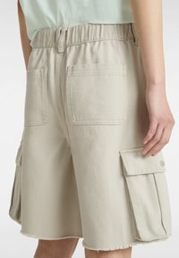 Beige cargoshorts i bomullsblandning, med elastisk midja, bakfickor och sidofickor med knappstängning. Fransad nederkant.