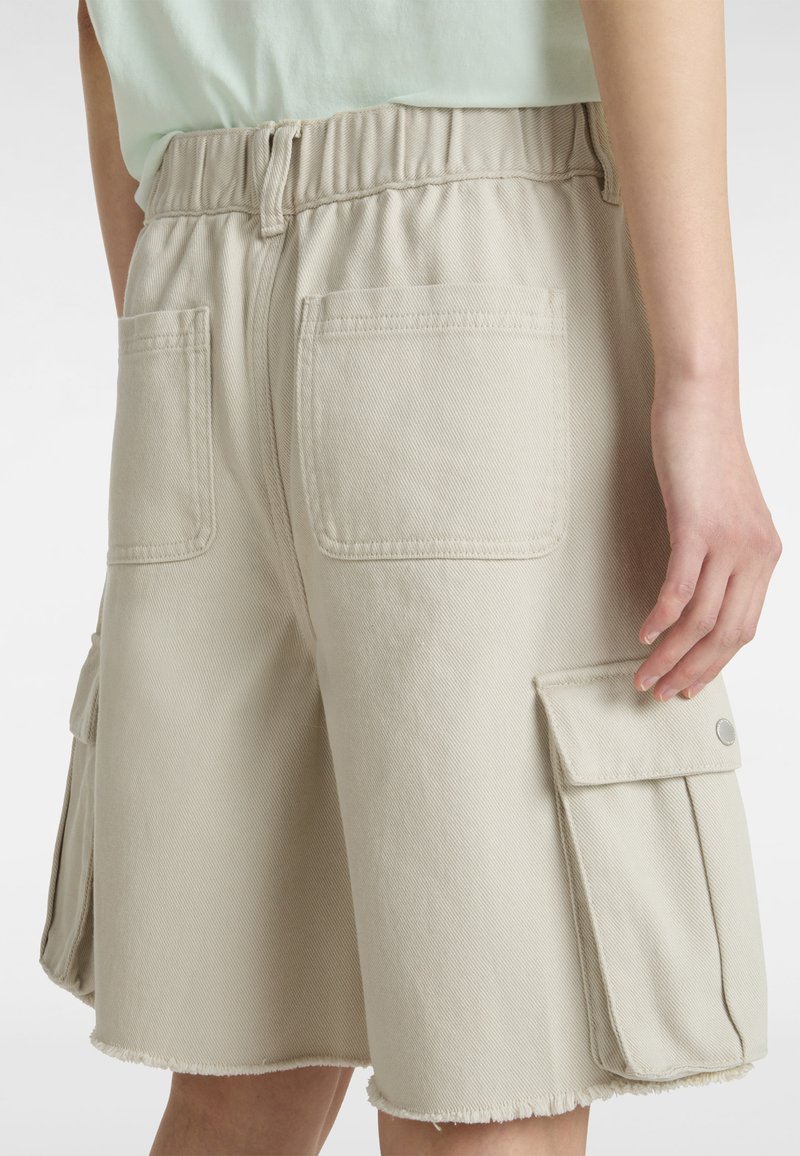 Pantalones cortos cargo en color beige, fabricados en una mezcla de algodón, con cintura elástica, bolsillos traseros y bolsillos laterales cargo con cierres de botón. Dobladillo deshilachado.