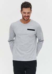 Szara, długosługa koszula z miękkiego materiału, z okrągłym dekoltem i kieszonką na piersi w czarnym akcentem. Minimalistyczny design.